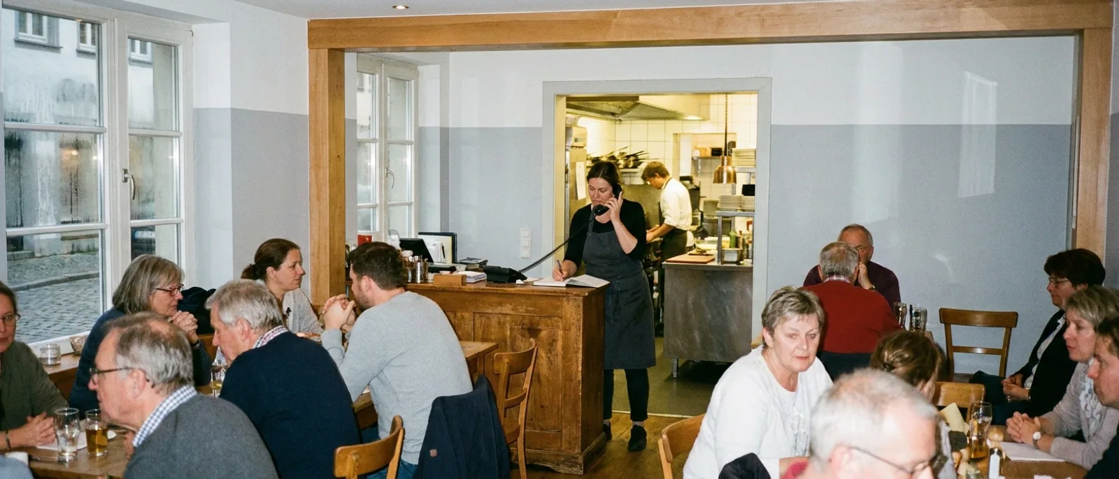Ein Restaurant im Service: volle Tische, während eine Mitarbeiterin am Telefon eine Reservierung aufnimmt.